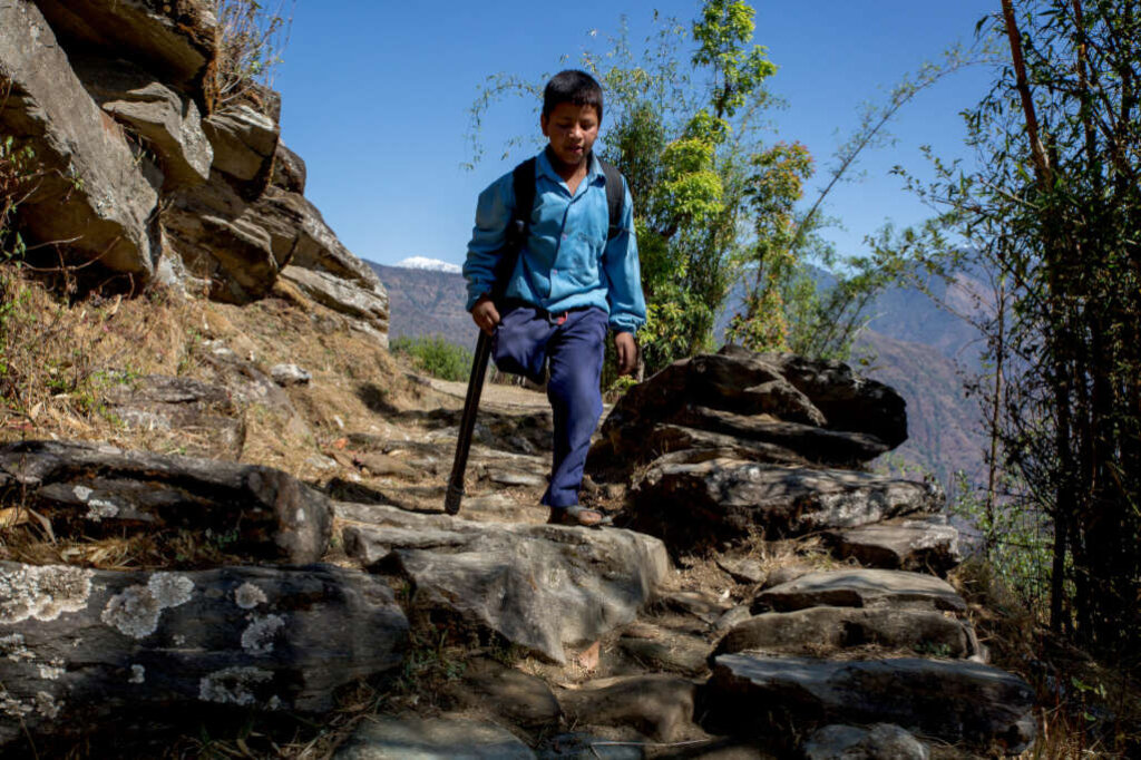 Bambino senza gamba destra scende da dirupo con aiuto di una stampella