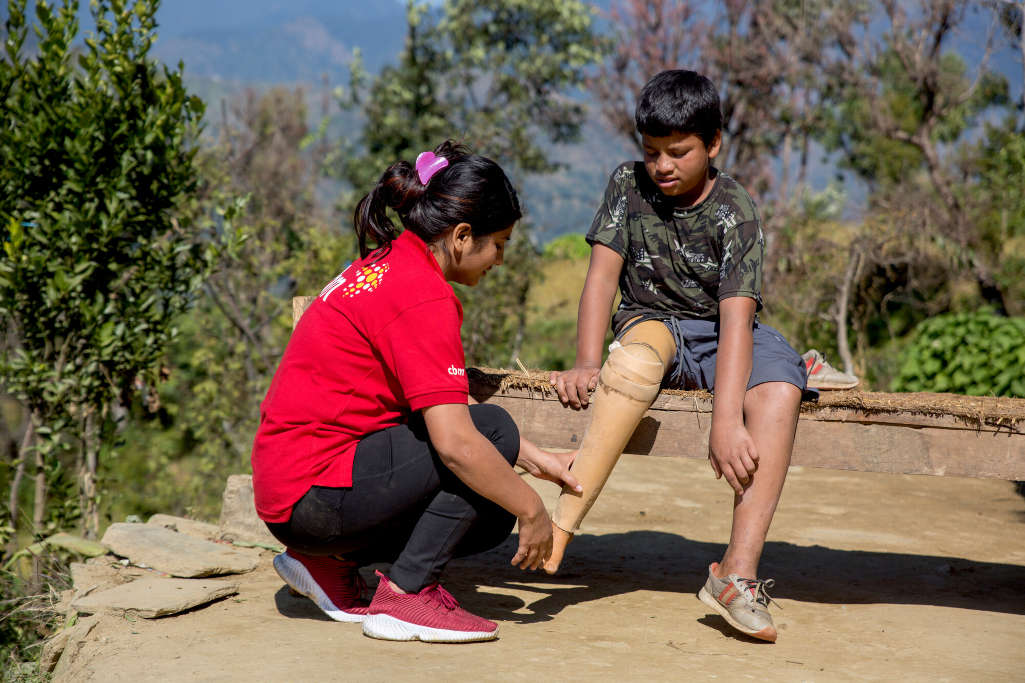 Operatrice con maglia rossa controlla protesi di Naresh, seduto sulla panca