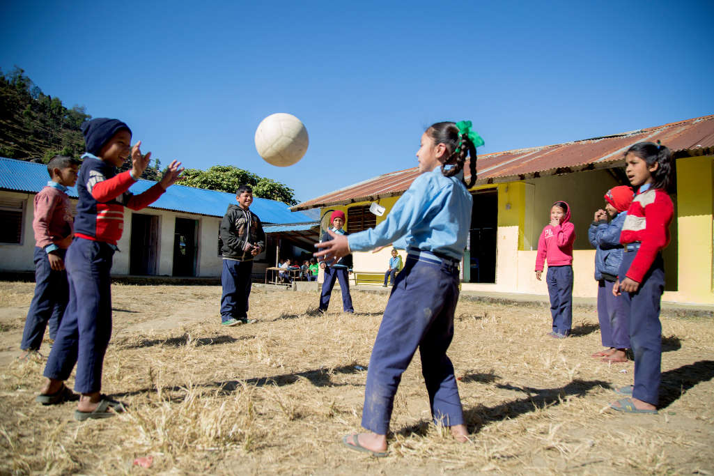 Bambini in cerchio si passano la palla. Indossano tutti la divisa, pantaloni blu e camicia azzurra, alcuni sopra indossano felpe o maglioncini.